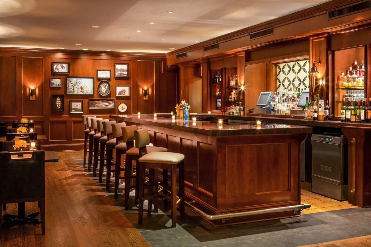 A stylish interior bar scene, accented by a gleaming bar counter, modern framed artwork, and warm lighting. Guests are seen socializing, celebrating, and enjoying a relaxed evening, capturing the spirit of community and festivity.