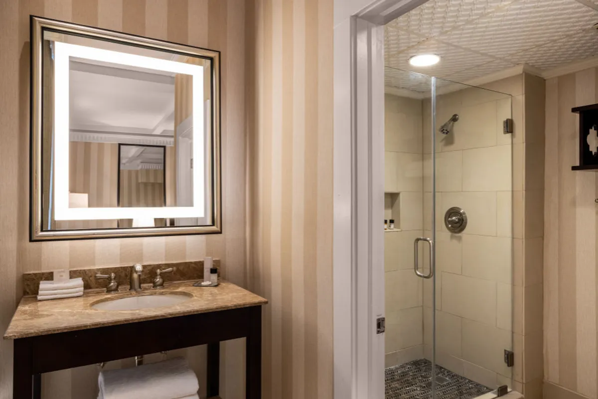 A sophisticated bathroom interior featuring an illuminated mirror, sleek vanity with sink, and a glass shower enclosure. The space exudes calm elegance, with upscale fixtures designed for comfort and rejuvenation.
